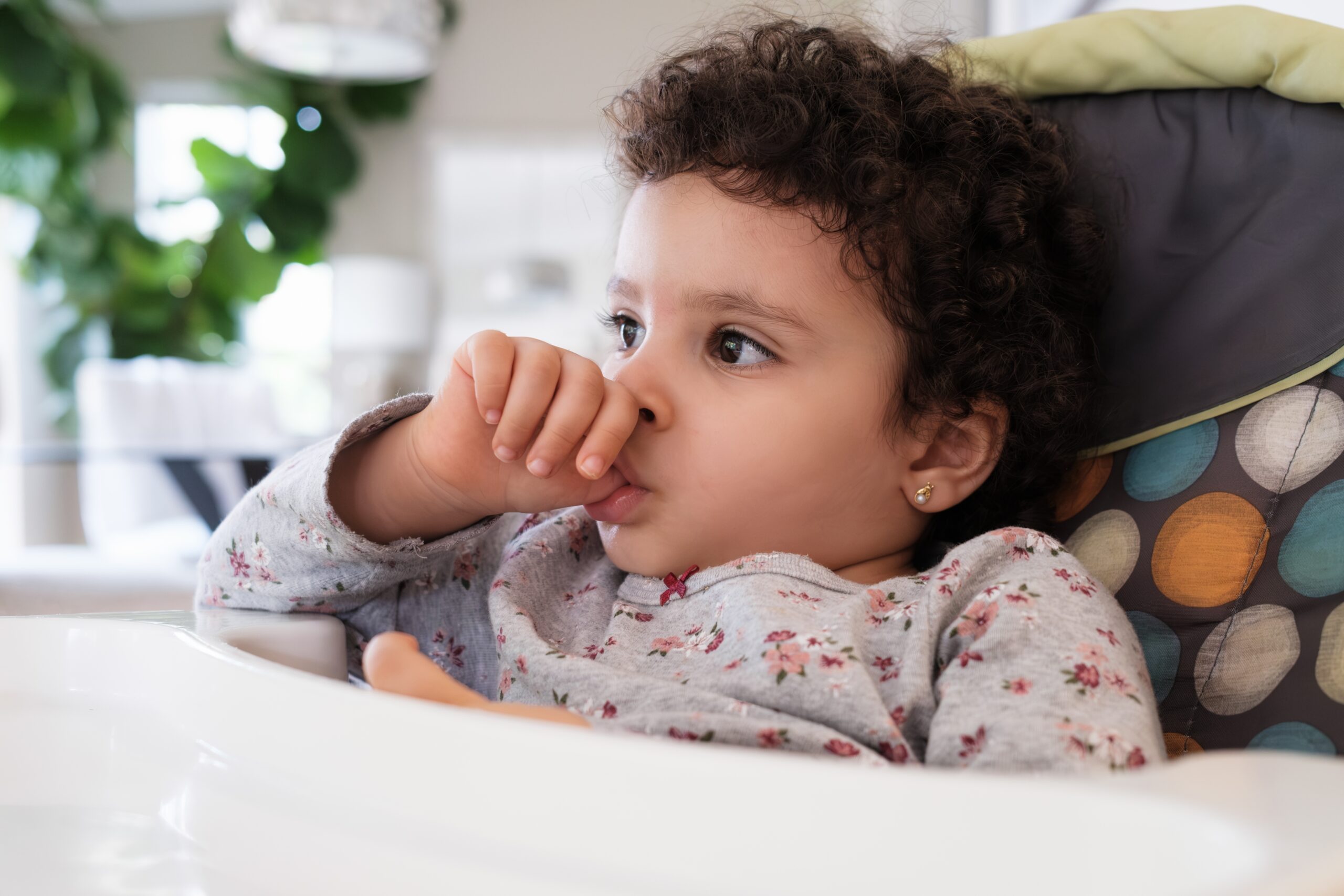 Child sucking thumb while seated in a high chair, reflecting common childhood habit discussed in relation to dental health and thumb sucking effects.