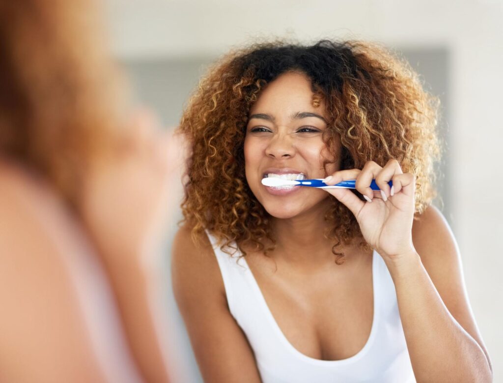 A woman brushing her teeth showing how to keep your braces clean.